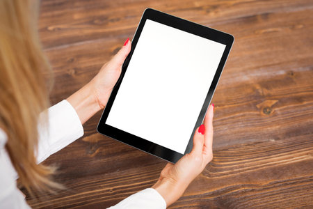 Woman holding tablet on wooden table.