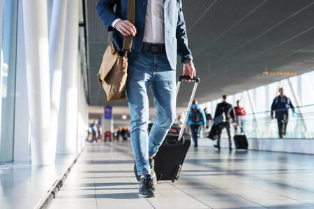 Man with shoulder bag and hand luggage walking in airport terminalの写真素材