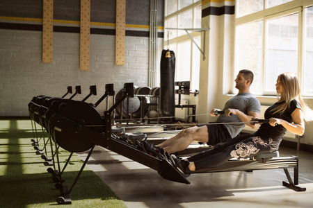 Man and woman training on rowing machines in gym together