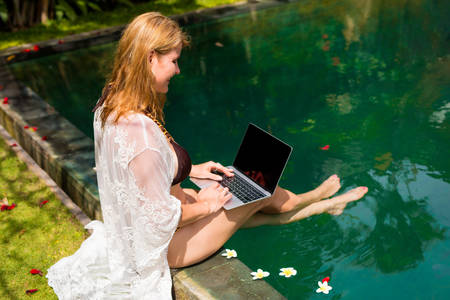 Woman relaxing by the pool and working with laptop computerの写真素材
