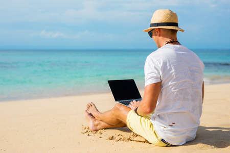 Casual looking guy using laptop on the beachの写真素材