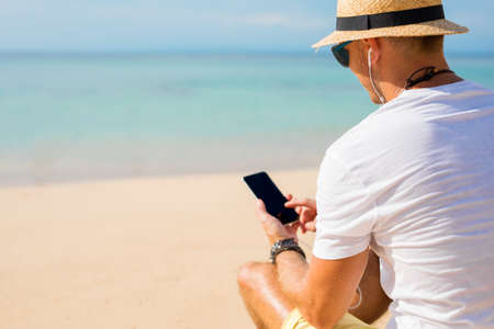 Guy using phone on the beachの写真素材