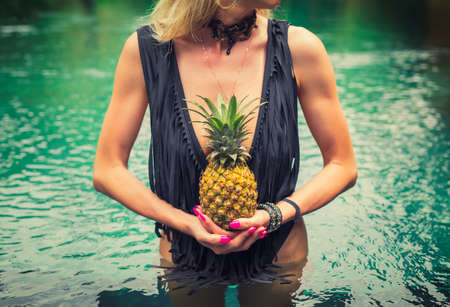 Woman standing in pool and holding pineapple in frontの写真素材