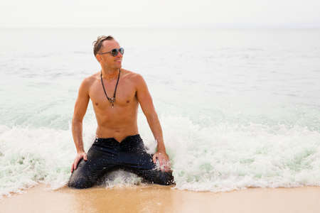 Man sitting in ocean in wet black jeansの写真素材