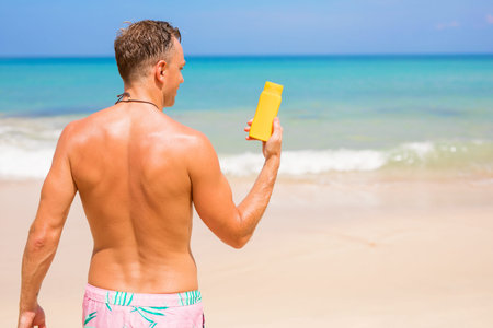 Man showing sun protection cream bottle on the beach