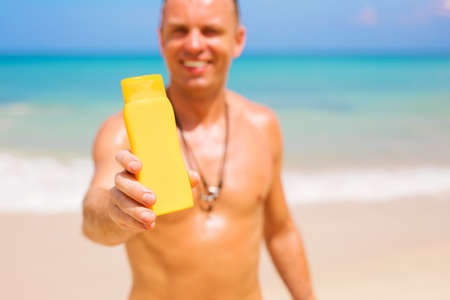Man holding sunscreen bottle on the beach. Focus on the sample product bottle.の写真素材