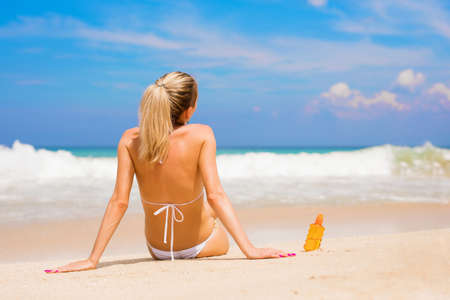 Woman sitting on the beach with sunscreen lotion bottleの写真素材