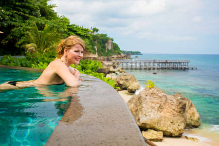 Woman enjoying ocean view from swimming poolの写真素材