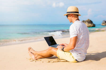 Young man working with laptop computer on the beachの写真素材