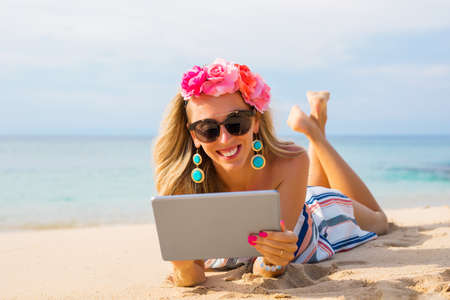 Cheerful young woman lying on the beach in sand and using tabletの写真素材