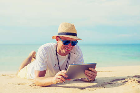Young handsome man using tablet on the beachの写真素材