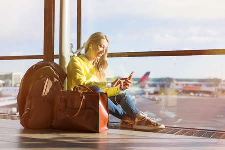 Woman sitting in airport and using her smartphoneの写真素材