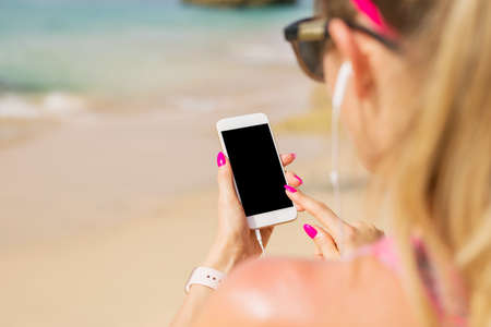 Woman holding mobile phone in hand and listening to music on earbudsの写真素材
