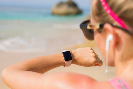 Woman with earphones looking at smartwatch while listening to music on the beachの写真素材