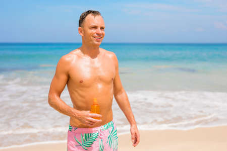 Man on the beach in bright sun holding sunscreen bottle in handの写真素材