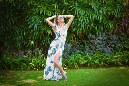 Woman in summer dress posing on green foliage backgroundの写真素材