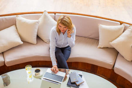 Busy businesswoman working with laptop and talking on phone, view from aboveの写真素材