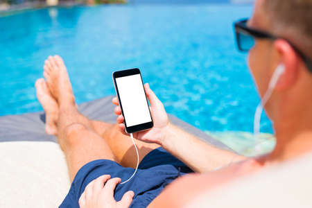 Man listening to music and holding mobile phone in hand by the pool.の写真素材