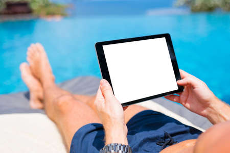 Man using tablet on vacation by the pool. Digital tablet mockup, horizontal screen orientation.の写真素材