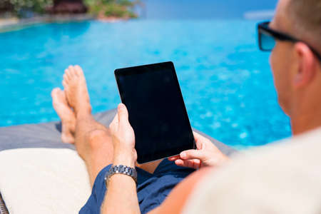 Man looking at tablet computer while sunbathing by the pool.の写真素材