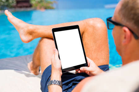 Man using tablet on vacation by the pool. Digital tablet mockup, vertical screen orientation.の写真素材