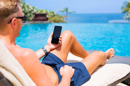 Man holding mobile phone while relaxing by the pool.の写真素材