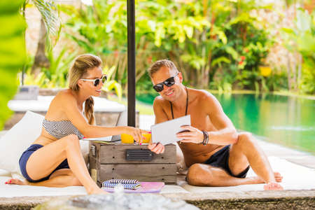 Woman and man looking at tablet while relaxing outside by the poolの写真素材