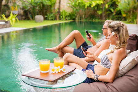 Couple using their mobile phones by the poolの写真素材