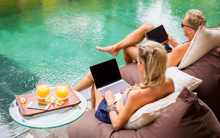 Couple sitting by the pool and using laptop computersの写真素材