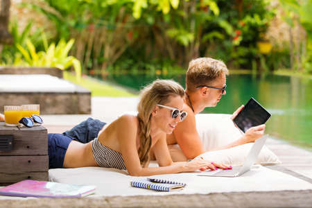 Woman and man lying in sofa next to swimming poolの写真素材