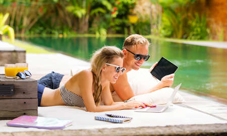 Couple with computers relaxing in sofa by the poolの写真素材