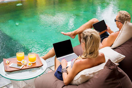Couple chilling by the pool and working on computersの写真素材