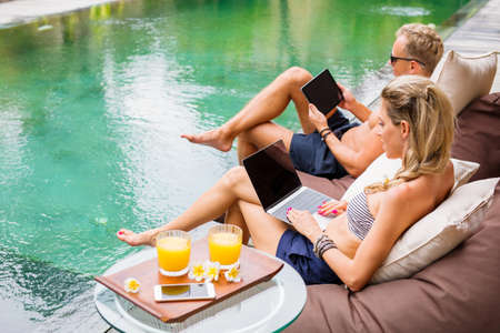 Couple working with computers while on vacation by the poolの写真素材
