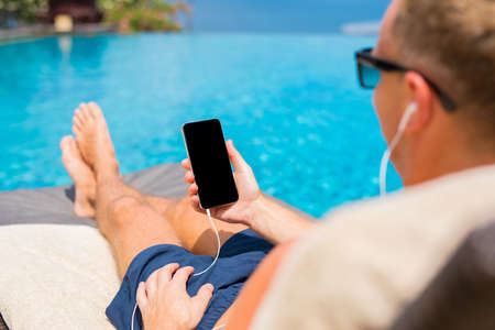 Man listening to music on phone by the poolの写真素材