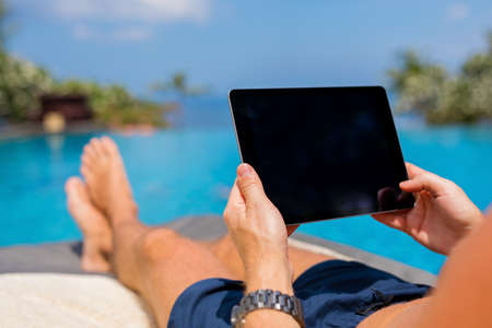 Man using digital tablet by the poolの写真素材