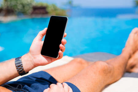 Man holding phone on vacation by the poolの写真素材