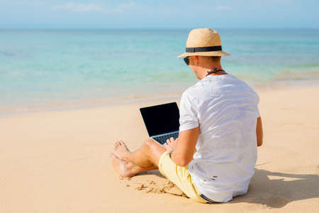 Relaxed man working with laptop on the beachの写真素材