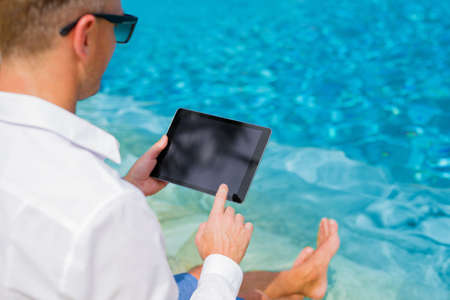 Businessman with tablet sitting by the poolの写真素材