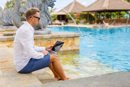 Man working on laptop by the poolの写真素材