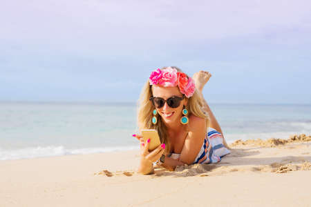 Young woman lying on the beach and using mobile phoneの写真素材