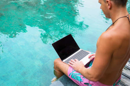 Man working on laptop while sitting by the poolの写真素材