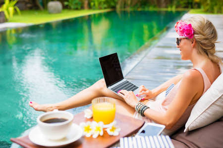 Woman working on laptop while sitting by the poolの写真素材
