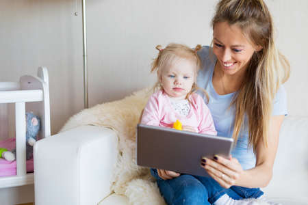 Mother showing something on tablet to her young daughterの写真素材