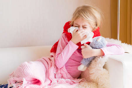 Sick girl with runny nose sitting in sofaの写真素材