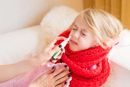 Mother treating her child's runny nose with nasal sprayの写真素材