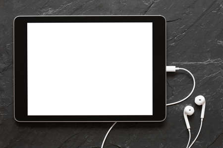 Tablet with empty screen and earphones on black stone surfaceの写真素材