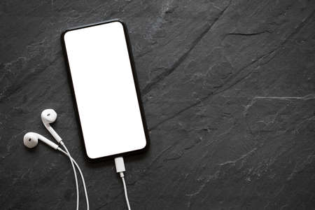 Mobile phone with empty screen and earphones on black stone surfaceの写真素材