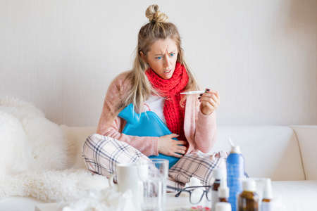 Sick woman measuring temperature with thermometerの写真素材