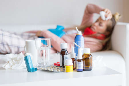 Sick woman lying in bed with many medicines on table in frontの写真素材