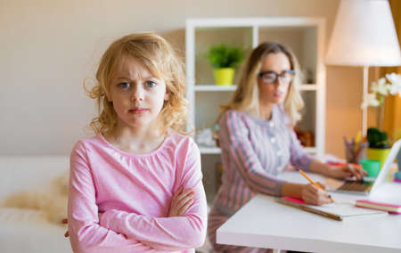 Sad girl standing next to her working motherの写真素材